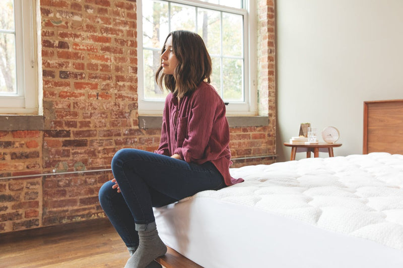 woman sitting on corner of bed with anti-static pad in place.